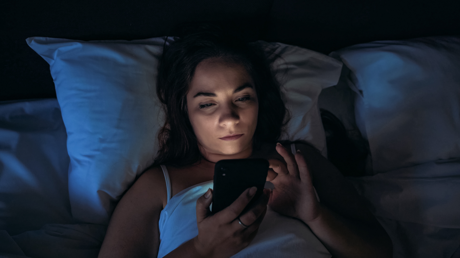 Jovem mulher deitada na cama olhando para o celular de noite